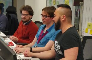 Haur Kang, performance analyst, sitting at desk discussing data visualisation needs with two team colleagues as they view laptops.