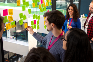 Some people stood in a semi circle looking at a window onto which post-it notes have been added