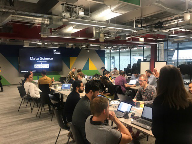 Groups of people sat on desks coding on laptops