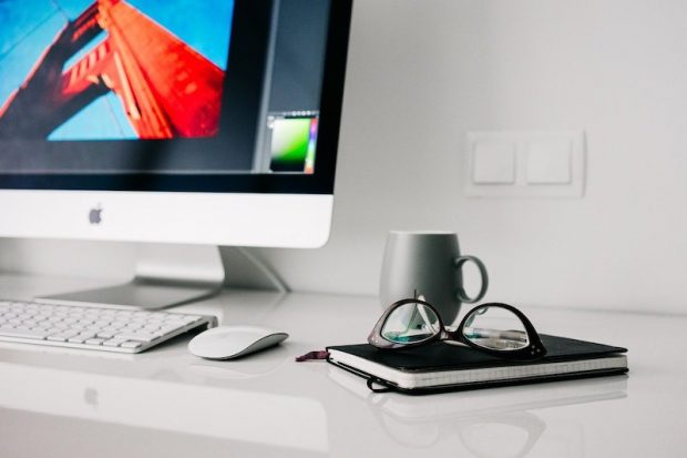 Image of a home office, with mouse, notebook and spectacles next to a Mac computer