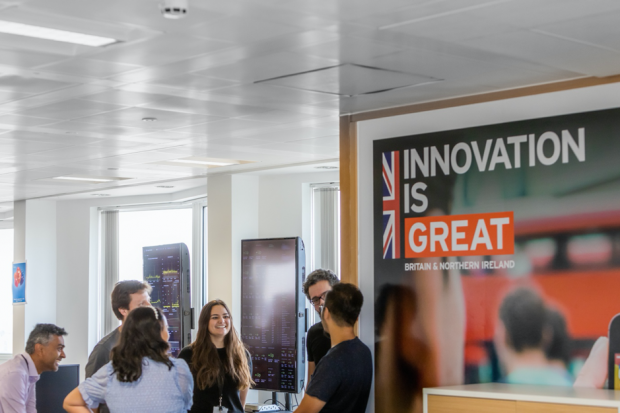 People having an informal stand-up meeting, next to a large 'Innovation is Great' poster