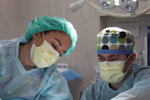 Photo of man and woman, perofrming surgery in surgical scrubs and faskmasks