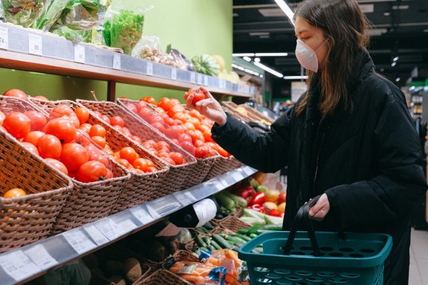 Woman wearing a facemask, shopping for tomatoes in a supermarket