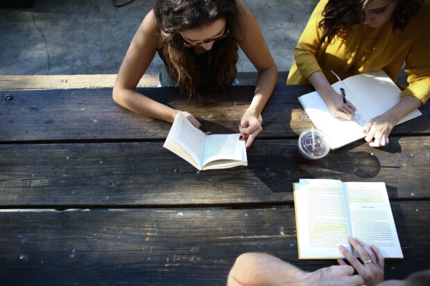 three people sat on a bench reading books and taking notes. Photo by Alexis Brown on Unsplash